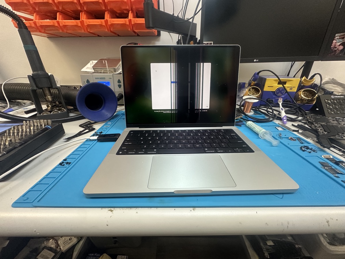 MacBook Pro with severe LCD damage showing vertical bars and lines on blue repair mat